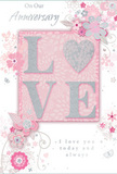 The anniversary card shown here is styled with the soft romance of a pastel floral design, evoking the gentle calm you might feel walking past the flowerbeds near Beckton's lakes and green spaces. At its core, the word LOVE appears in bold, raised lettering, each letter coated in a fine mix of blush-pink, pearl-white, and subtle silver glitter. The surface of the letters has a tactile, almost velvety texture, catching and reflecting the light with a gentle shimmer that feels reminiscent of candlelight on a quiet evening at home. Encircling this central word is an intricate pattern of stylised flowers and flowing foliage, illustrated with delicate lines in shades of pink, ivory, and pale grey. The blossoms are slightly abstract, their petals and centres defined with fine shading that suggests softness and depth rather than strict realism. Slender vines and leaves twist and curl around the flowers, some touched with silver detail, creating an airy frame that leads the eye gracefully around the card. The background is a smooth, blush-pink hue, providing a warm, intimate atmosphere and allowing the glitter and silver to stand out without appearing harsh. Tiny flourishes-small swirls, scattered dots, and barely-there buds-add a sense of lightness, as if petals were gently drifting across the surface. An elegant, script-style font carries heartfelt anniversary words, placed so they sit comfortably within the floral design, never overwhelming it. The overall effect is one of tender celebration and enduring affection, like a thoughtfully chosen bouquet delivered by a local Beckton florist to mark a shared journey of love and commitment.